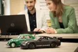 twee mensen bekijken financial lease for you website op computer met twee miniatuur autootjes op voorgrond